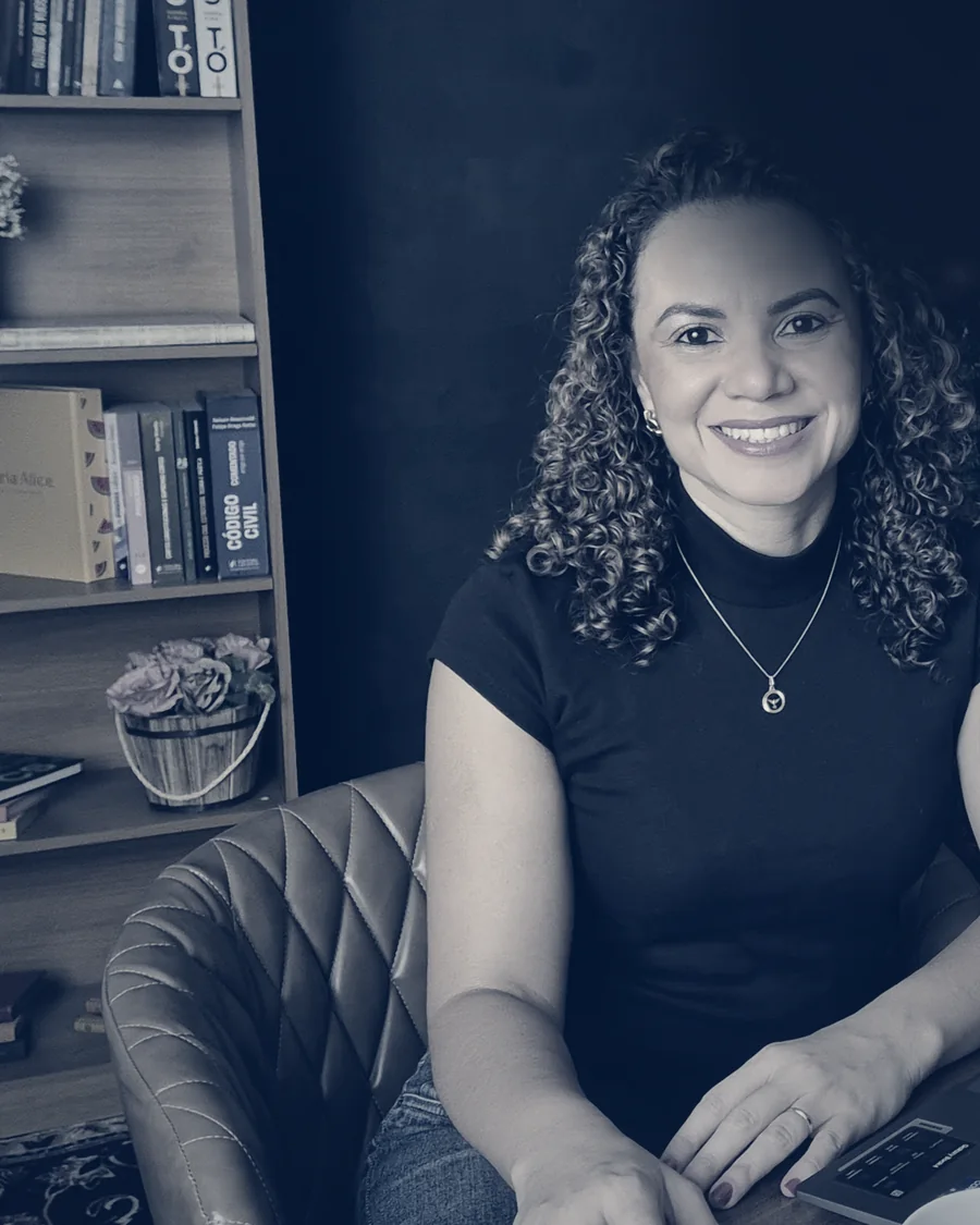 Manuella Santana, sorrindo, sentada em seu escritório diante de uma estante de livros